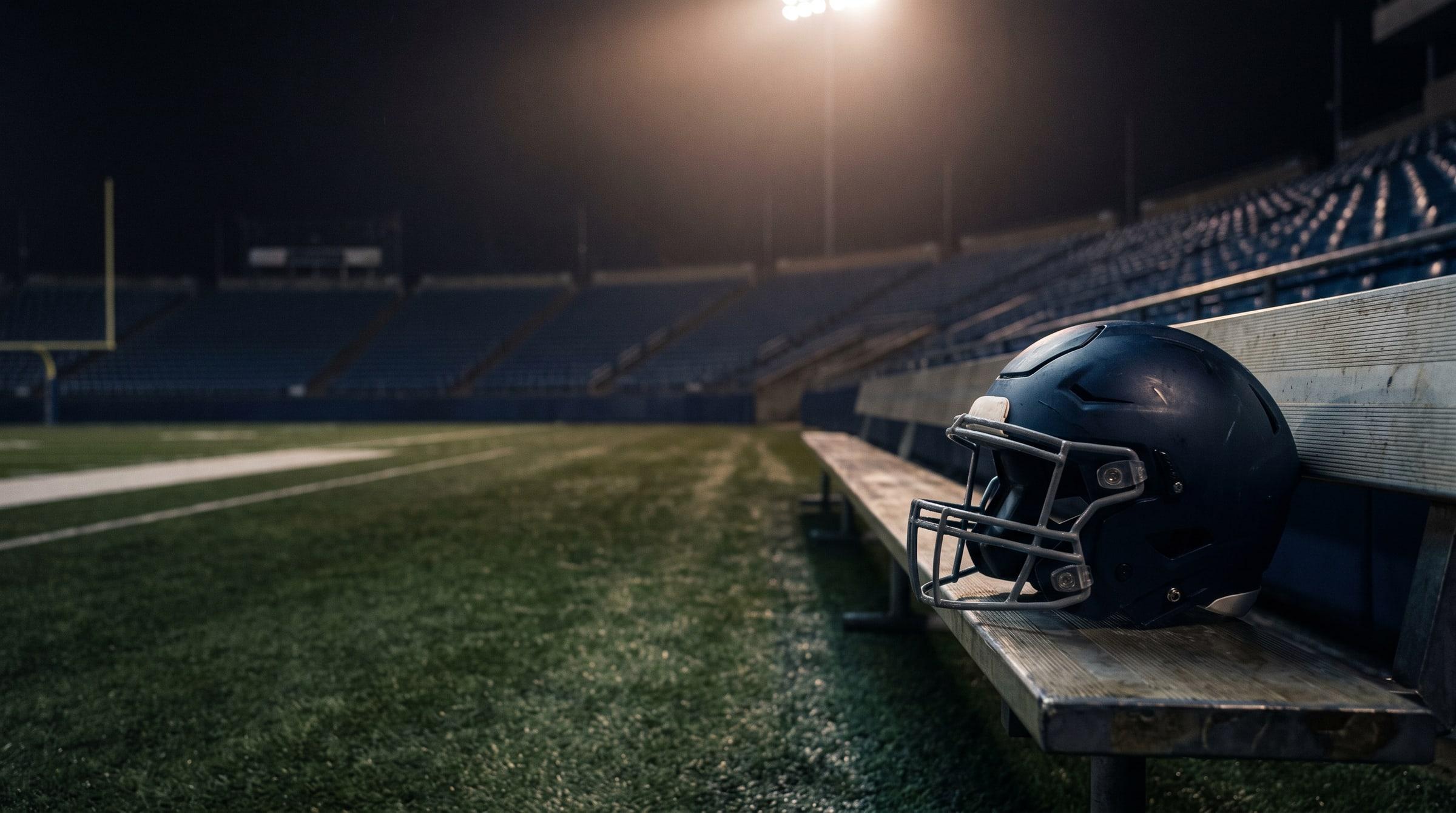 A worn football helmet rests on a sideline bench in an empty stadium after the final whistle